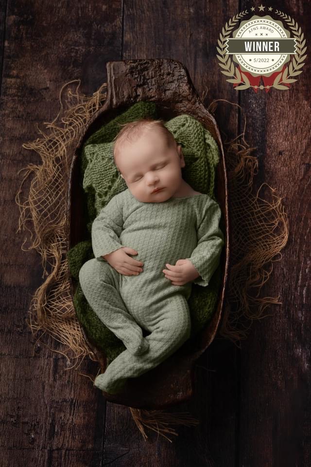 newborn baby boy in a green outfit lay down in a dark brown bowl on dark brown wooden floor.  Taken by newborn photographer Sutton Coldfield birmingham