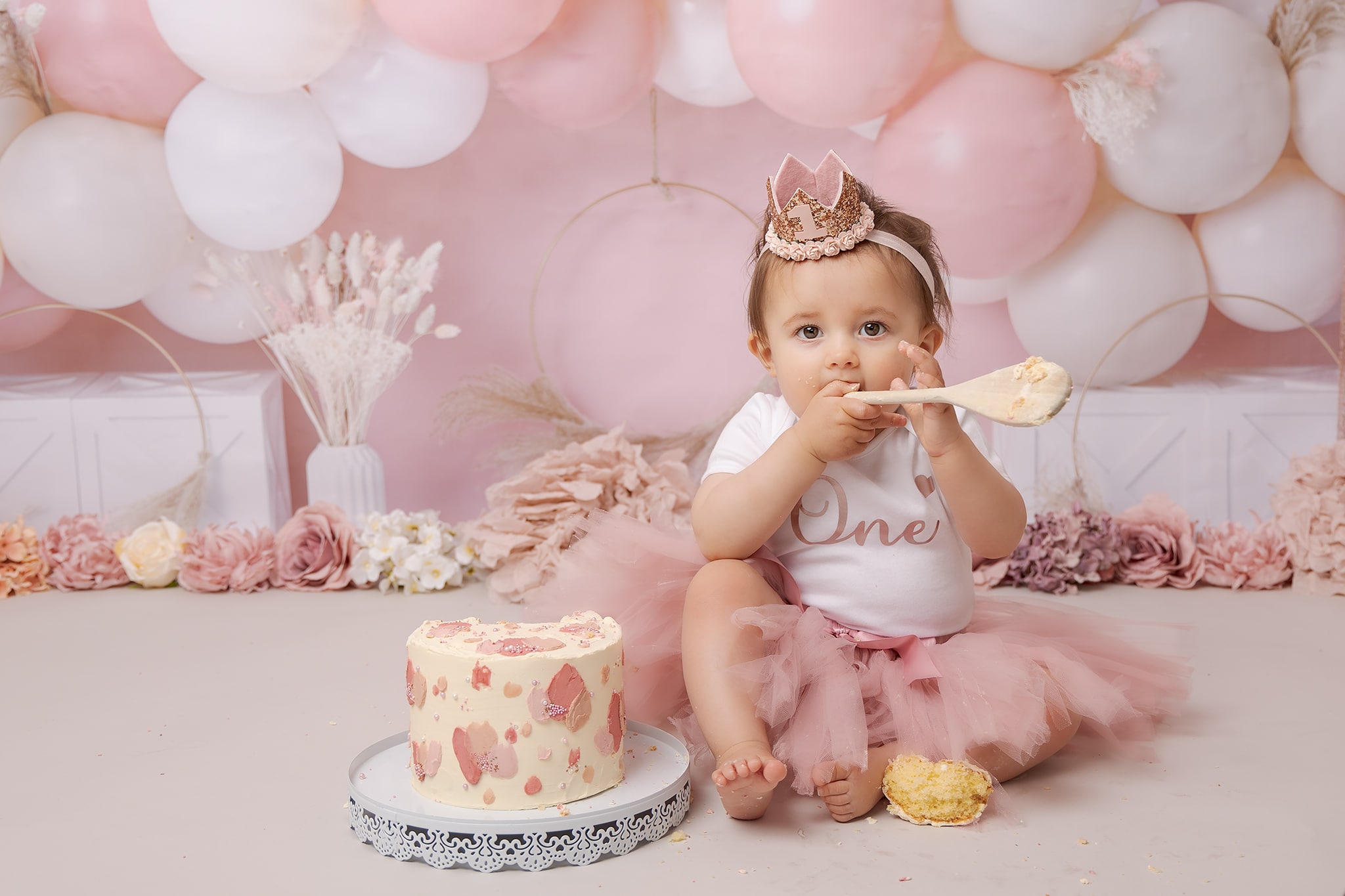 one year old with wooden spoon ready to smash her cake, during her cake smash photoshoot in Sutton Coldfield Birmingham 
